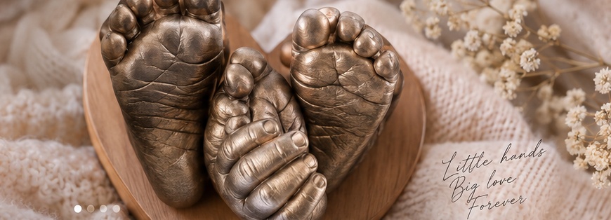 Bronze baby foot and hand castings on a wooden display, surrounded by soft knit fabric